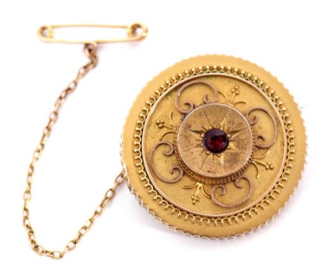 Victorian gold circular target brooch centring a small round garnet in a starburst engraved setting, raised in an Etruscan su