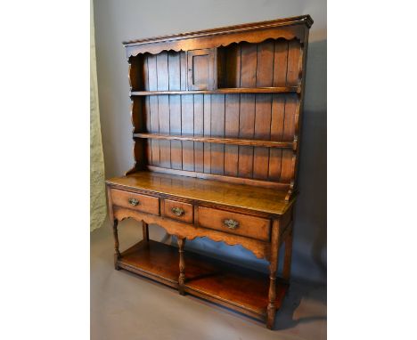 A Green Oak Dresser, the boarded shelf back with spice cupboard above three drawers raised upon turned legs with under tier, 