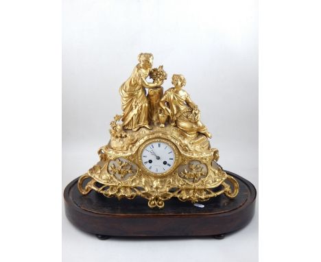 A late 19th century gilt metal mantel clock, cast with two women seated beside a stump, the white enamel dial set out in Roma