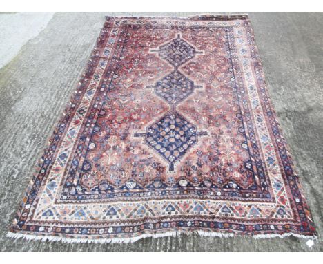 A handmade woollen rug with a light red ground. With three blue ground shapes to centre, richly decorated with stylised birds