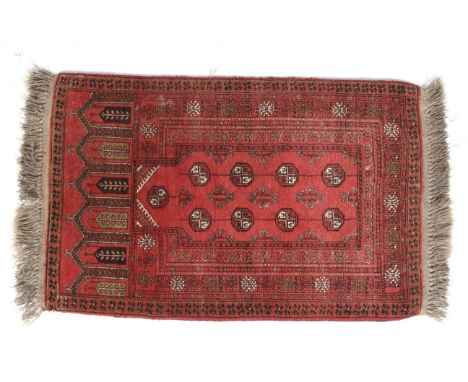 A small red ground prayer rug. With shaped central ground pointing towards a row of architectural shapes, with details in bla