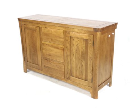 A contemporary solid blonde oak sideboard. With a central three drawer section flanked by single door cupboards, each with an