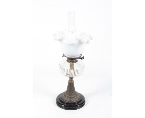 A Victorian brass oil lamp. With a clear glass reservoir, on a tapered stand with scroll decoration, mounted on a black ceram