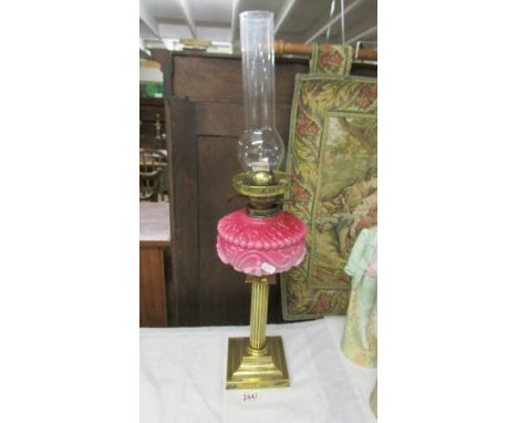 A Victorian brass oil lamp with reeded column, pink glass font and complete with burner and chimney.