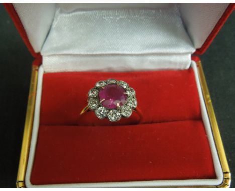 AN EDWARDIAN RUBY AND DIAMOND CLUSTER RING.  The central ruby measuring approximately 7mm in diameter surrounded by ten old c