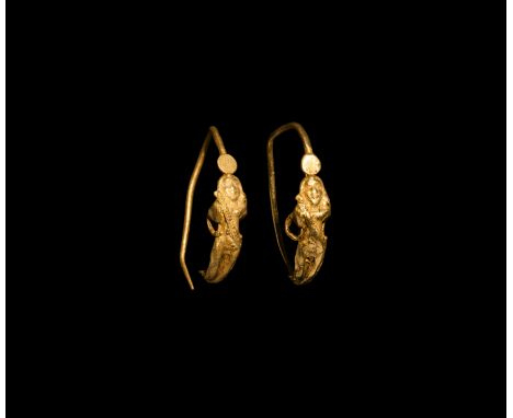 5th-3rd century BC. A matched pair of gold earrings, each a slender hoop with applied figure of Eros standing nude with hands