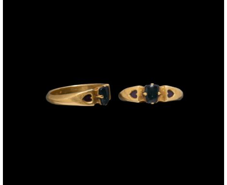 Mid 14th-mid 15th century AD. A gold finger ring with D-section hoop, flared and cusped shoulders each with an inset garnet a