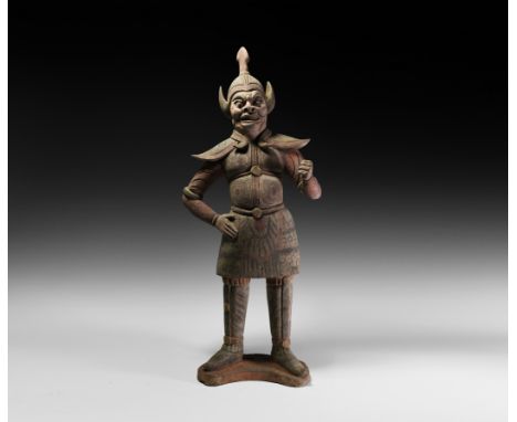 Tang Dynasty, 618-906 AD. A ceramic figure modelled standing on a crescent-shaped base; the guard wears an aggressive facial 