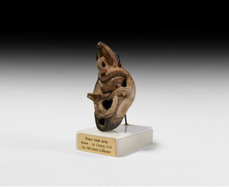 1st-2nd century AD. A terracotta oil lamp shaped as a head of a comic actor wearing a mask of a satyr or slave; thick hair, k