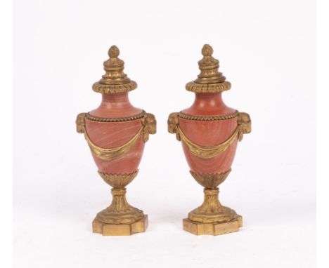 A pair of French ormolu mounted rouge marble cassoulet urns, with fruiting finial, rams mask and swags, on shaped quatrefoil 