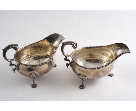 A PAIR OF EARLY 20TH CENTURY SAUCE BOATS on three scroll legs with shell feet, gadrooned borders & leaf-capped, flying scroll