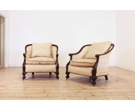 A pair of large carved mahogany low bergère chairs,first half of the 20th century, each with crisply carved arms terminating 