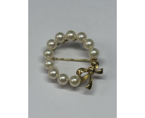 AN 18CT GOLD AND PEARL BROOCH BY MIKIMOTO, WITH ELEVEN UNIFORM PEARLS SET IN A CIRCULAR BROOCH WITH BOW DETAIL AND GOLD PIN, 