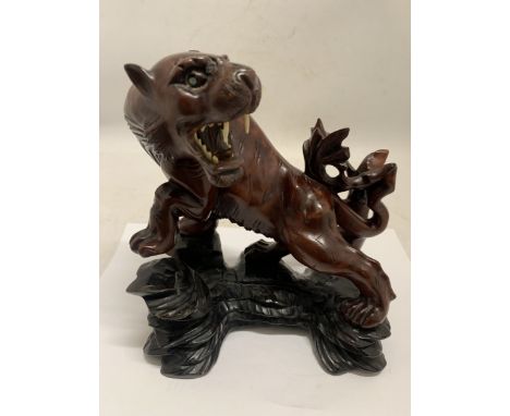 A CHINESE HAND-CARVED WOODEN TIGER STATUE WITH GLASS EYES - 19 CM (H) 18 CM (L)
