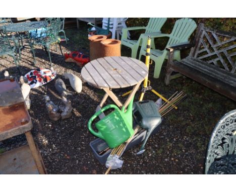 A wooden folding garden table; a tripod stand; two watering cans; a plant trough; and garden canes 