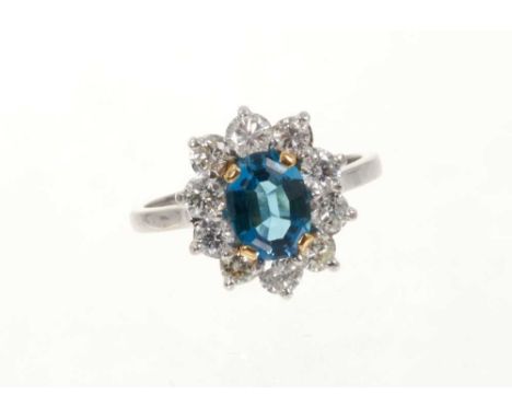 Diamond and blue topaz cluster ring with a central oval mixed cut blue topaz surrounded by a border of ten brilliant cut diam