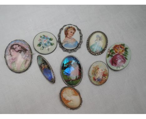 Eight brooches of various forms including cameo, ceramic, butterfly wing and enamelled all having silver mounts and a similar