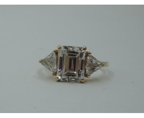 A synthetic clear three stone dress ring having a central emerald cut stone flanked by two trillion cut stones in a claw set 