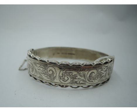 A silver hinged bangle having decorative edging and engraved scrolling. Approx 30.4g