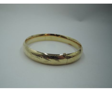 A yellow metal hinged bangle stamped 14K having slide clasp and engraved decoration, approx 13.5g