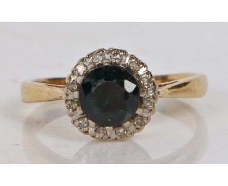 An 18 carat gold, sapphire and diamond ring, the central circular facet cut sapphire surrounded by a band of diamonds, ring s