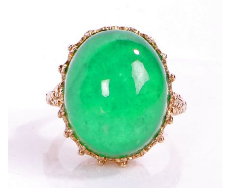 An impressive jade and yellow metal ring, the head set with a large claw mounted cabochon cut jade stone set on a elaborate m