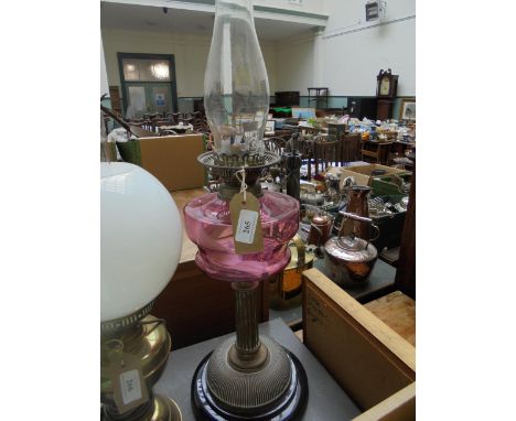 Paraffin lamp with cranberry glass bowl supported by brass corinthian column on circular black pot base