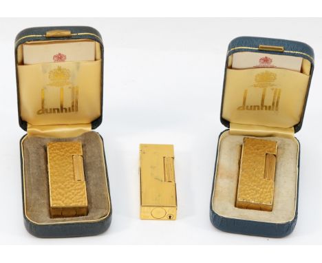 Alfred Dunhill; Three Dunhill rollagas pocket cigarette lighters, two gold plated with bark effect decoration, cased with ins