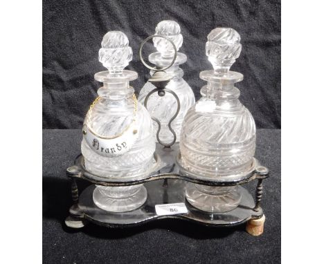 AN EARLY VICTORIAN PAPIER MACHE SPIRIT DECANTER STAND with a set of three cut-glass spirit decanters and a 'Brandy' label