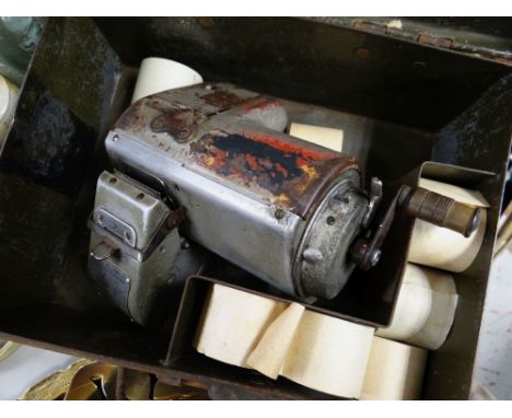 A vintage Mycalex bus ticket machine together with a selection of ticket rolls in a metal tin