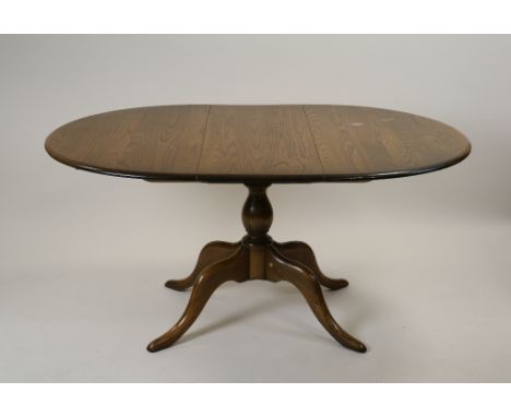 An Ercol elm extending D-end pillar dining table with extra leaf on a baluster turned column and four down curved tapering le
