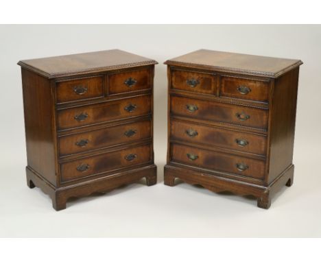 A pair of George III style crossbanded mahogany small chests of two short and three long cockbeaded drawers on shaped aprons 