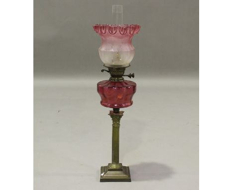 A late 19th/early 20th century brass and cranberry glass table oil lamp, fitted with a frosted pink glass shade, height 67cm,