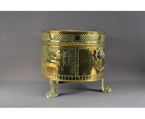 A large brass footed planter, twin handled, with loops and lion heads, decorated with people in natural surroundings, raised 