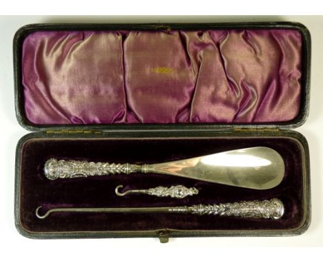 A late Victorian cased silver handled shoe horn, button hook and later small button hook, all with decorative handles and in 