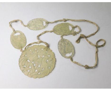 JADE. A late 19th century, Chinese carved &amp; pierced jade necklace on woven cord. Drop diameter 5.5.
