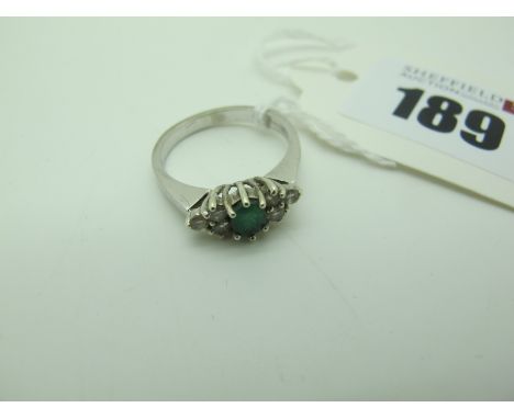 A 9ct White Gold Emerald and Diamond Set Dress Ring, oval claw set to the centre between six brilliant cut stones (finger siz