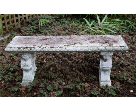 A CAST RECONSTITUTED STONE GARDEN BENCH with a rectangular top with egg and dart moulded edge and on winged rams supports, 12