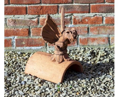 A CAST TERRACOTTA FINIAL in the form of a winged creature seated on half round ridge tile, the tile 30cm long, the creature a