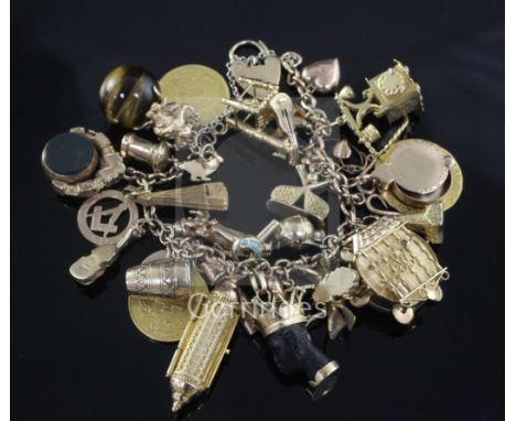 An early 20th century 18ct gold charm bracelet, hung with twenty seven assorted mainly 9ct gold charms, including spade guine