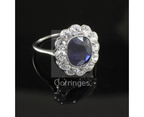 A white metal, sapphire and diamond oval cluster ring the central oval cushion cut sapphire bordered with twelve round cut di