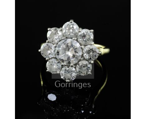 An 18ct gold and nine stone diamond cluster ring, the central round brilliant cut stone weighing approximately 1.50ct, size R