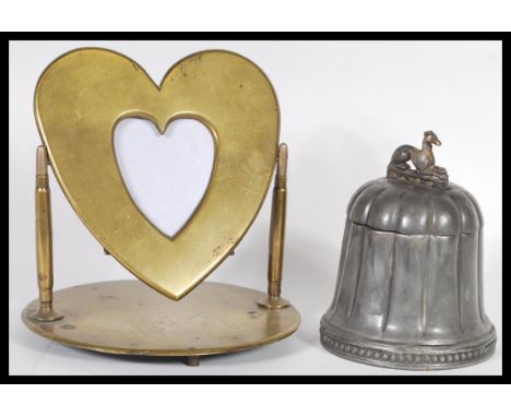 A 20th Century brass trench art swing photo frame in the form of a heart raised on a round base along with a pewter domed cad