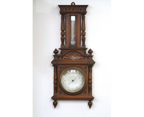 An Edwardian carved walnut aneroid barometer/thermometer, with profuse floral decoration, flanked by reeded columns and turne