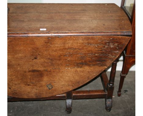 An Antique oak gate leg dining table, having rounded drop leaves, raised on turned columns united by stretchers and terminati