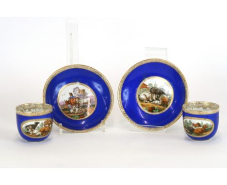 Four Meissen cups and saucers, decorated with panels of cattle and figures on a blue ground, heightened in gilt