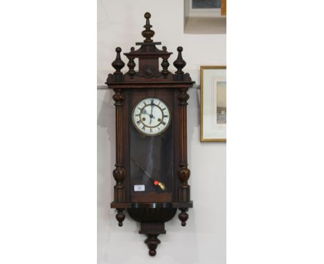 A Victorian walnut regulator type wall clock, with turned finials, glazed panel door enclosing a circular white enamel Roman 