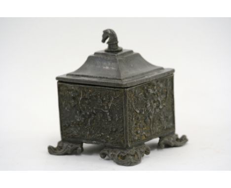 An antique lead tobacco box, decorated with scenes of hunting, the lid surmounted by a horses head and raised on scroll feet