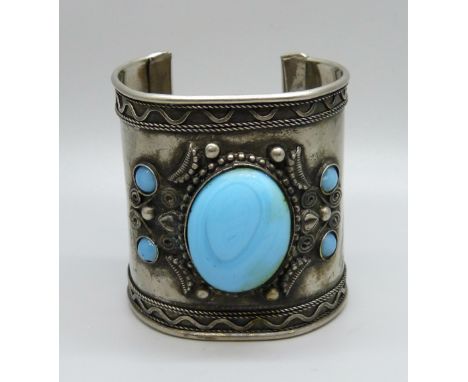 A large white metal bangle with blue stones 