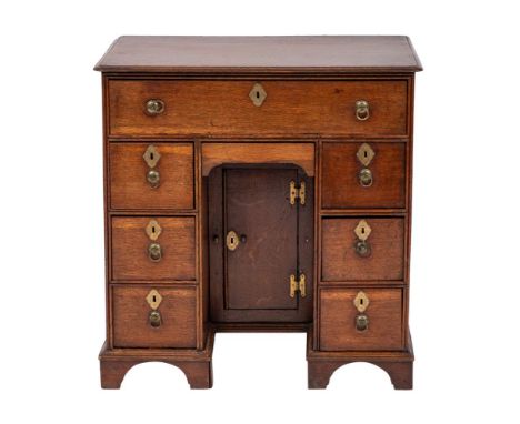 A George II oak kneehole desk, circa 1735,: the top with moulded front and side edges, above an arrangement of seven drawers 